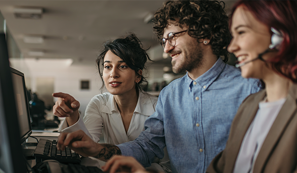 Time de colaboradores reunidos em frente a um computador. Imagem sinalizando alocação de profissionais de ti.